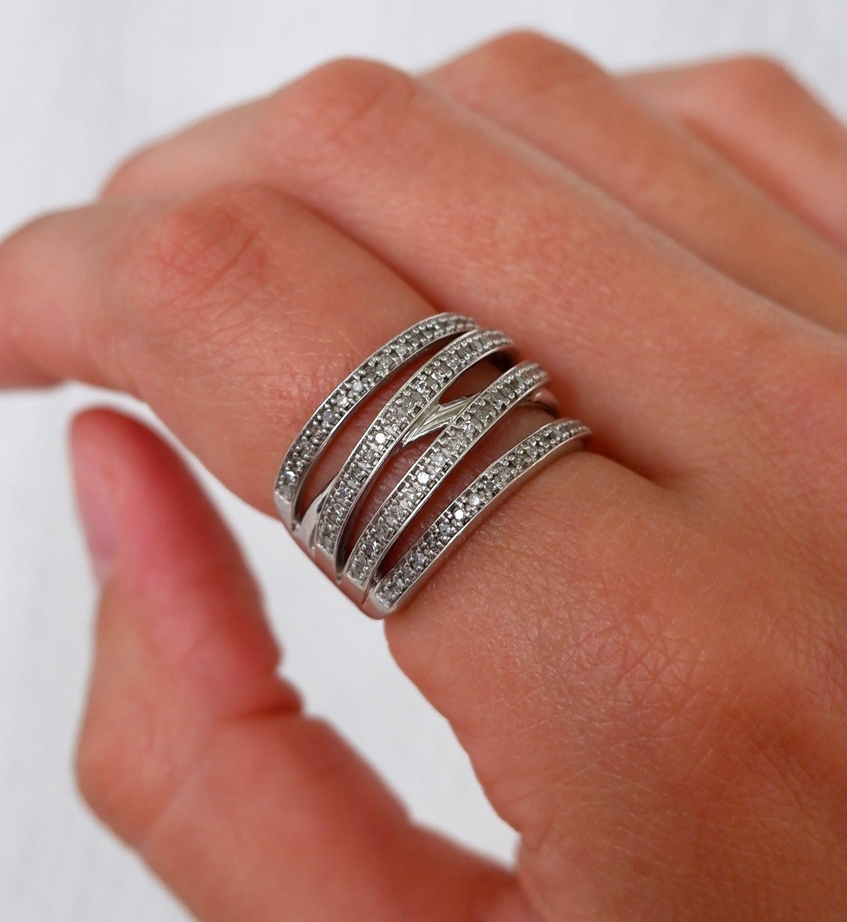 A close-up of a hand wearing a multi-band silver ring set with small clear stones, photographed against a soft light background.