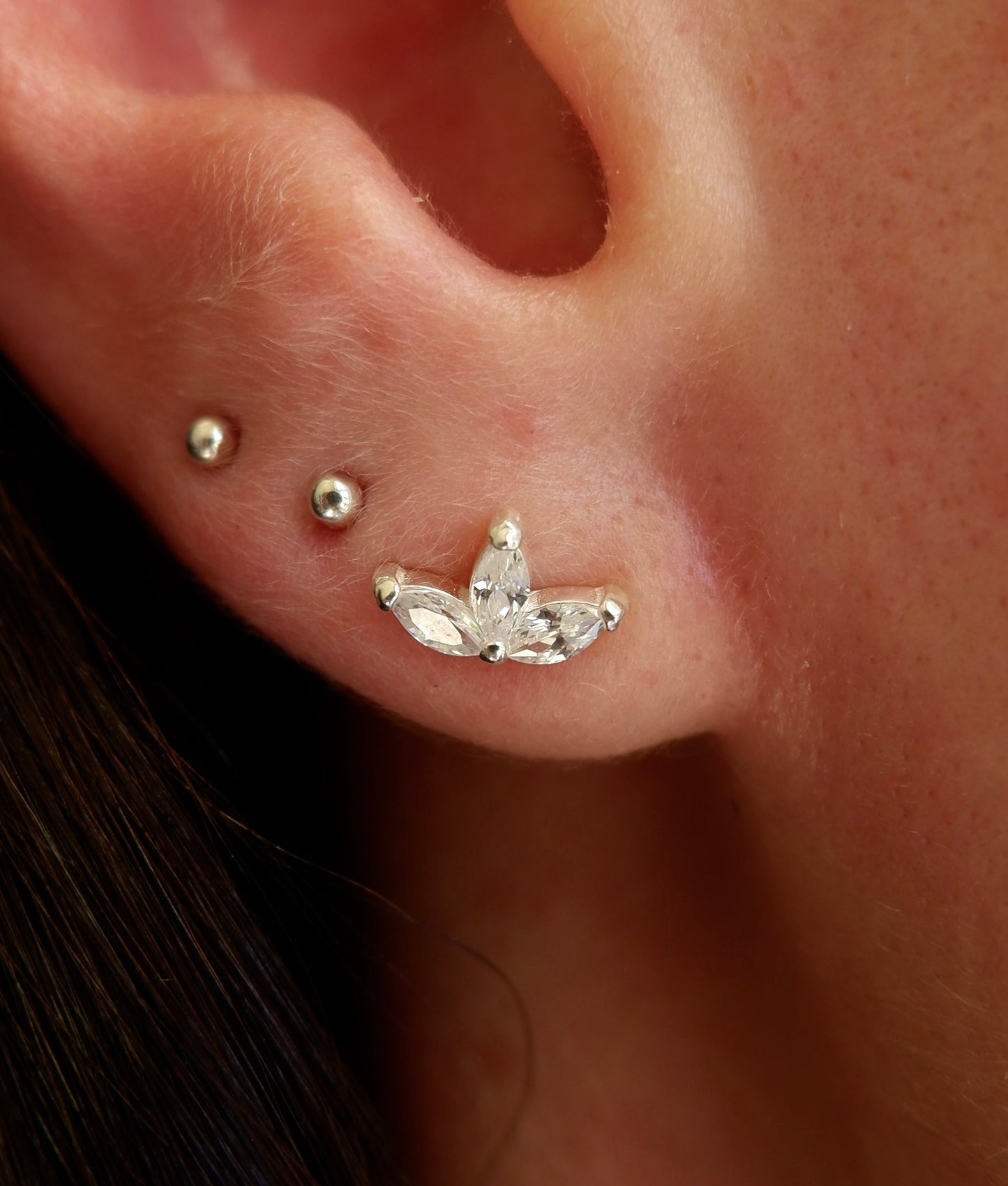 Close-up of an ear with a silver earring and two studs.
