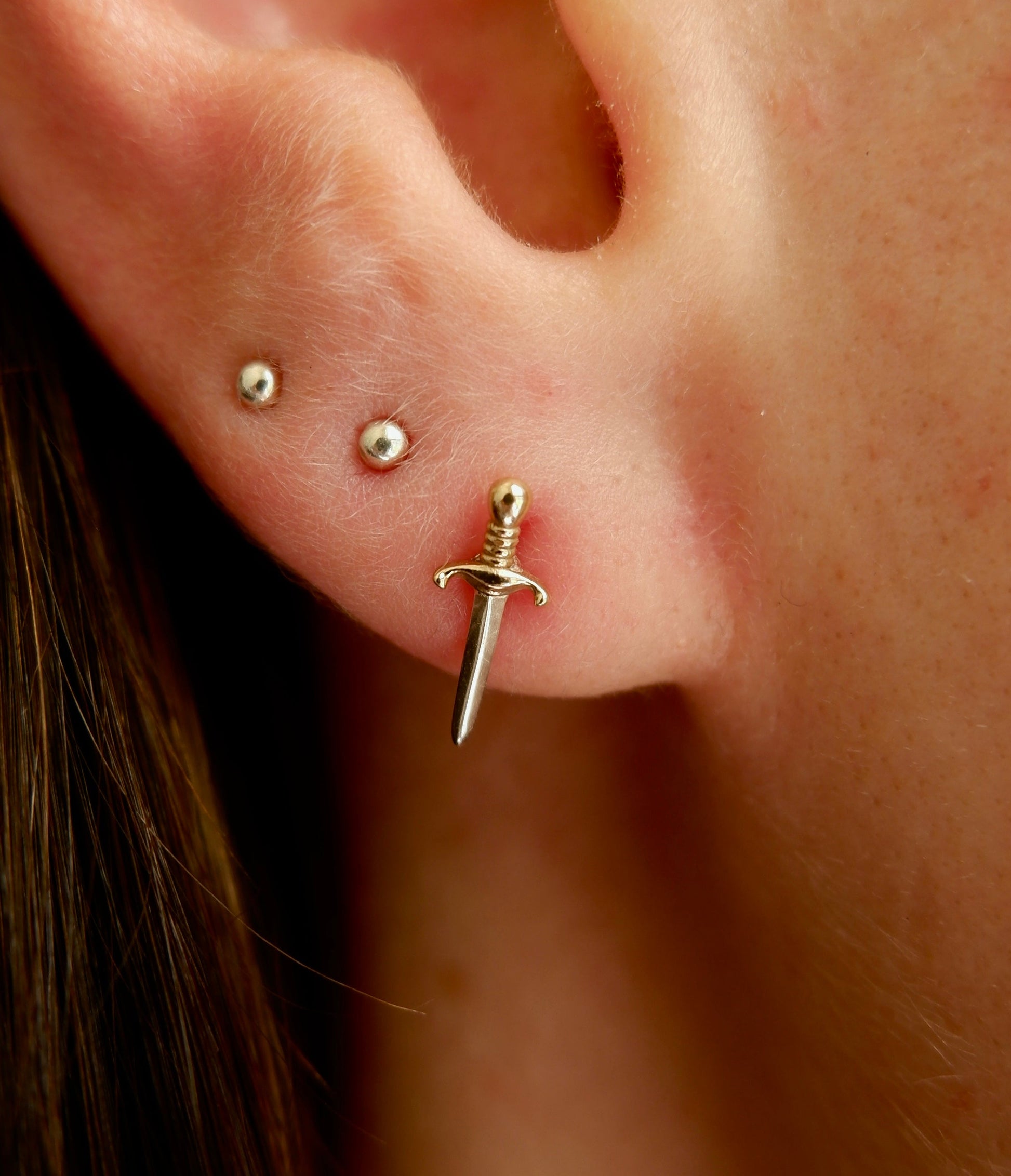 Close-up of an ear with a gold sword-shaped earring.