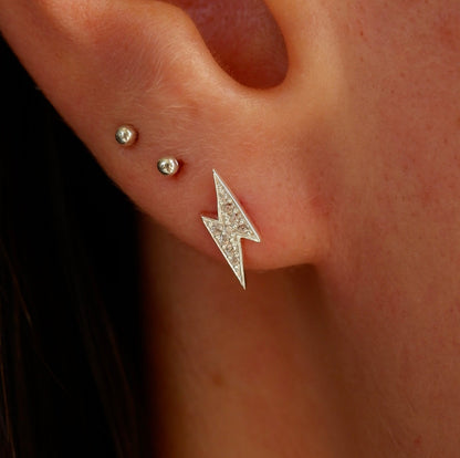 Close-up of an ear with a lightning bolt earring and two smaller studs.