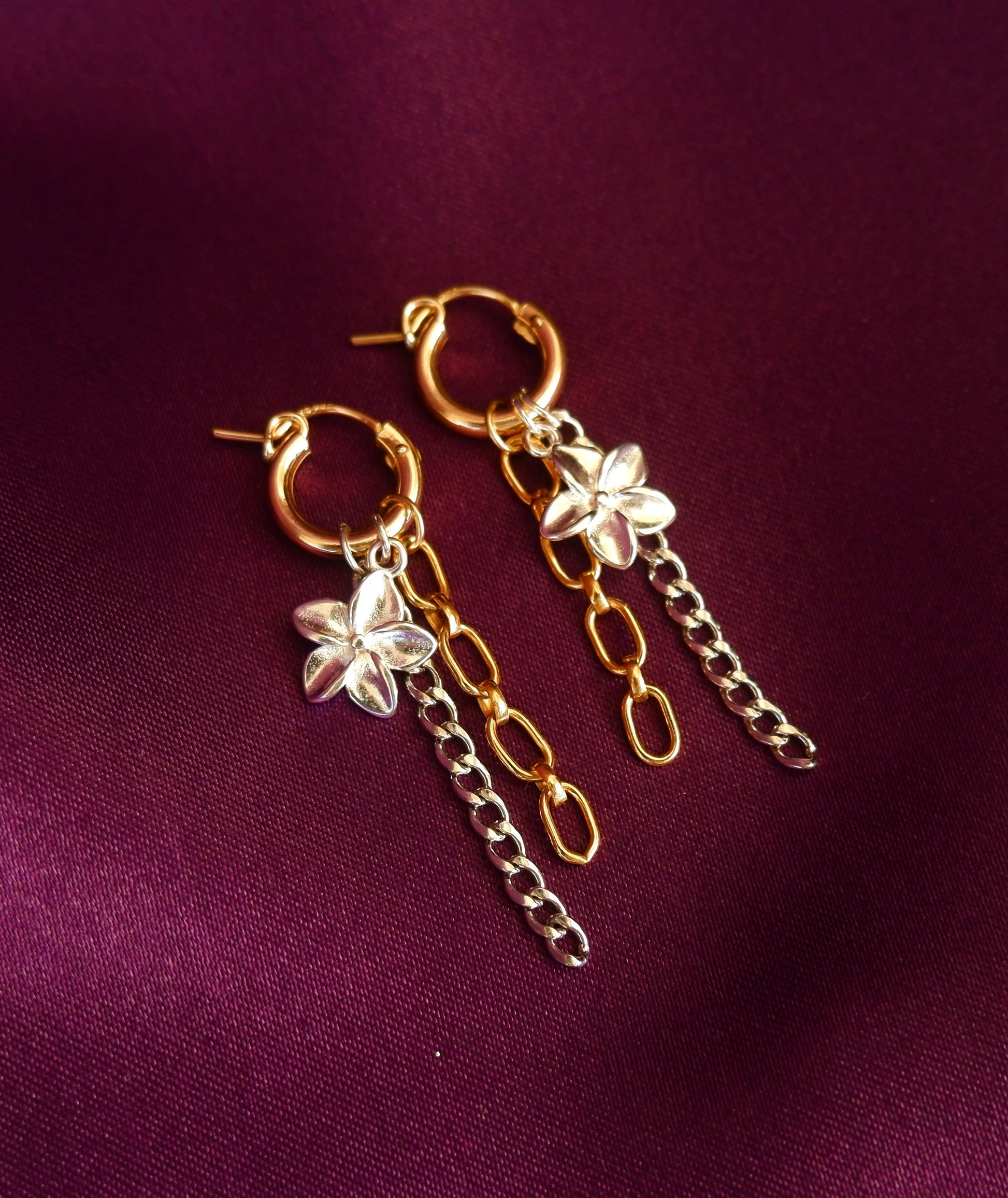 Gold hoop earrings with chain and floral charms on a purple fabric background