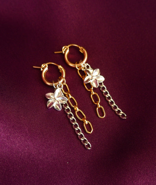 Gold hoop earrings with chain and floral charms on a purple fabric background