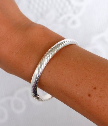 A close-up of a person's wrist wearing a silver bangle bracelet against a white textured background.