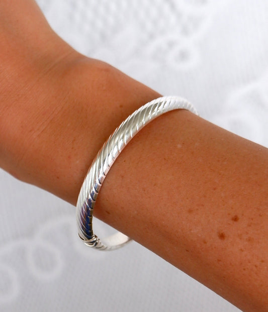 A close-up of a person's wrist wearing a silver bangle bracelet against a white textured background.