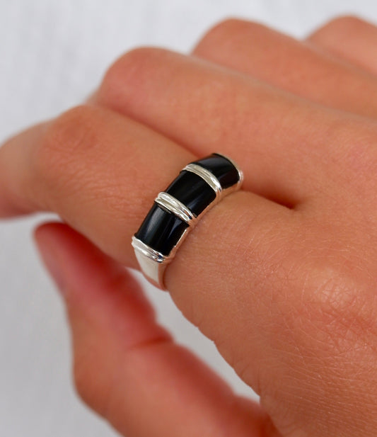 A close-up of a hand wearing a silver ring with three horizontal black inlay segments.